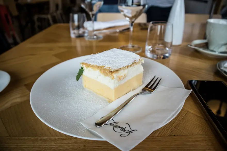 A slice of Bled kremšnita with a mint leaf, served on a white plate at a restaurant table