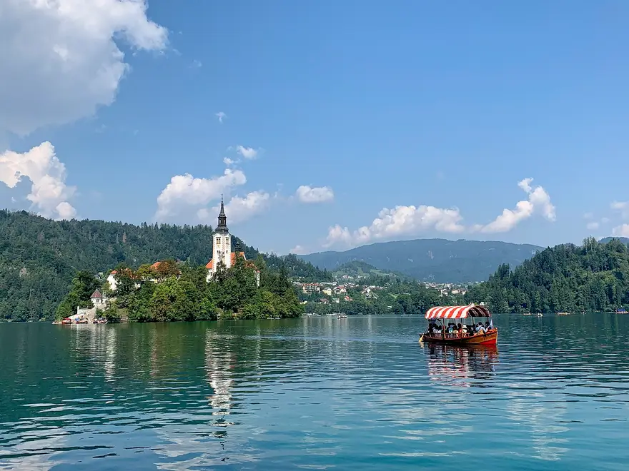A pletna boat crossing Lake Bled towards the island church on a summer day